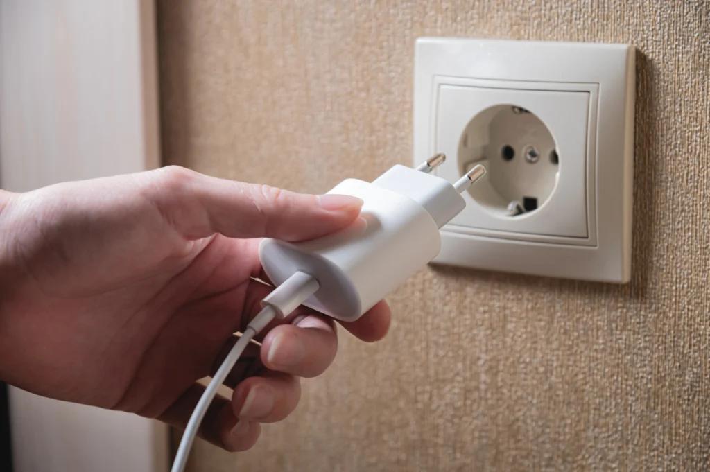 Pessoa conectando um carregador em uma tomada elétrica para carregar um dispositivo eletrônico em uma parede com tomada iluminada. Conteúdo sobre plugues e tomadas.
