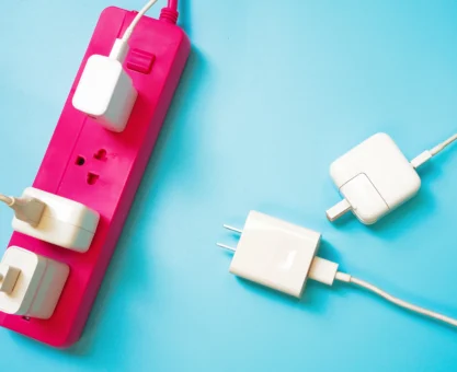 Fita extensora para tomada elétrica com três dispositivos conectados, incluindo carregadores e adaptadores, sobre fundo azul. Conteúdo sobre plugues e tomadas.