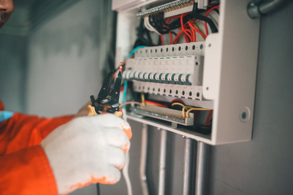 Técnico realizando manutenção elétrica em painel de controle, com ferramentas e componentes elétricos visíveis, em ambiente industrial, conforme normas abnt.