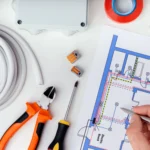 Ferramentas de elétrica e um projeto elétrico de instalação detalhado numa mesa de trabalho, conforme normas abnt.