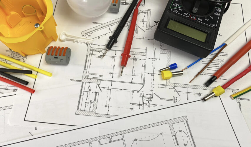 Técnico de manutenção verificando o projeto elétrico com diagramas elétricos em painel de controle de sistema industrial com componentes eletrônicos ao fundo.