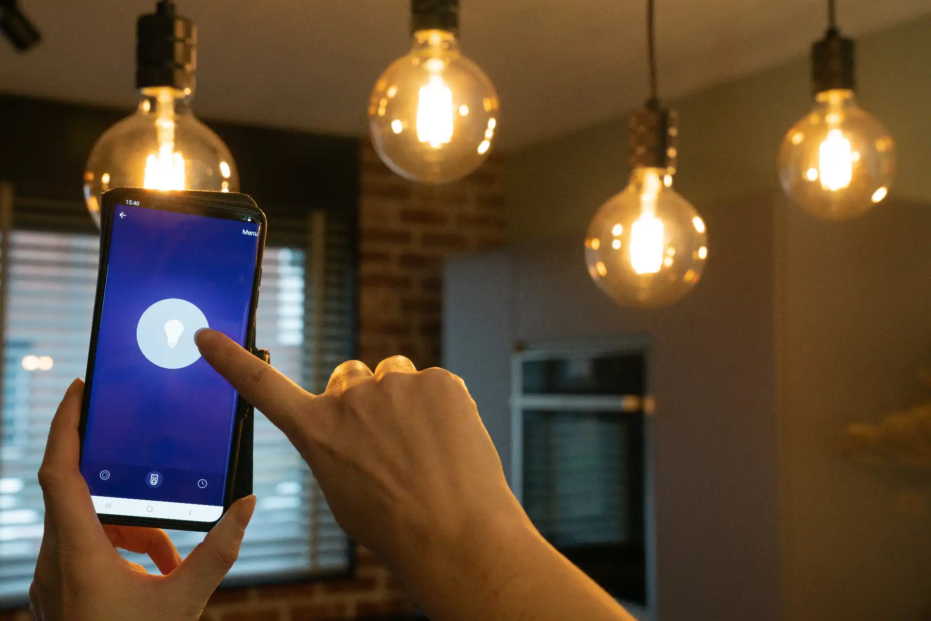 Pessoa interagindo com smartphone que exibe ícone de luz ou ideia, em ambiente moderno com iluminação de pendentes de vidro, dica sobre como economizar energia.