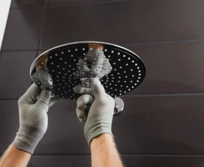 Instalação de um chuveiro Lorenzetti 220v de teto moderno em um banheiro com azulejos escuros, com mãos de trabalhador ajustando o equipamento.