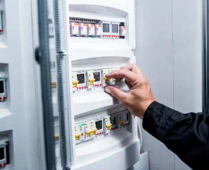Mão ajustando e removendo disjuntor em quadro elétrico industrial com módulos e identificações, ao lado de outros componentes de proteção em painel de energia