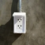 Imagem de tomada de sobrepor instalada em uma parede cinza para ilustrar o artigo da EletroNunes sobre o assunto.