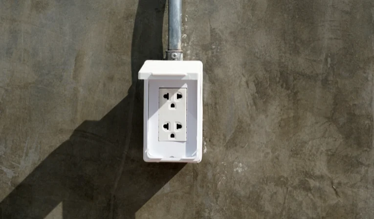 Imagem de tomada de sobrepor instalada em uma parede cinza para ilustrar o artigo da EletroNunes sobre o assunto.