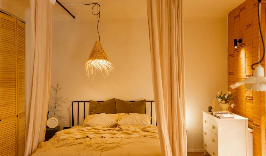 Iluminação no quarto com luminária pendente estilo cúpula de tecido sobre a cama, luz quente e cortinas claras, criando ambiente aconchegante e moderno.