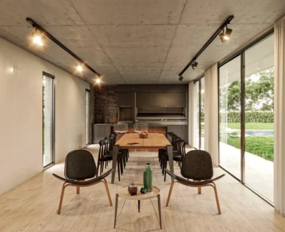 Ambiente externo moderno com mesa de jantar e poltronas, iluminação em trilho eletrificado preto no teto e refletor direcionável em fachada com grandes portas de vidro e jardim ao fundo.
