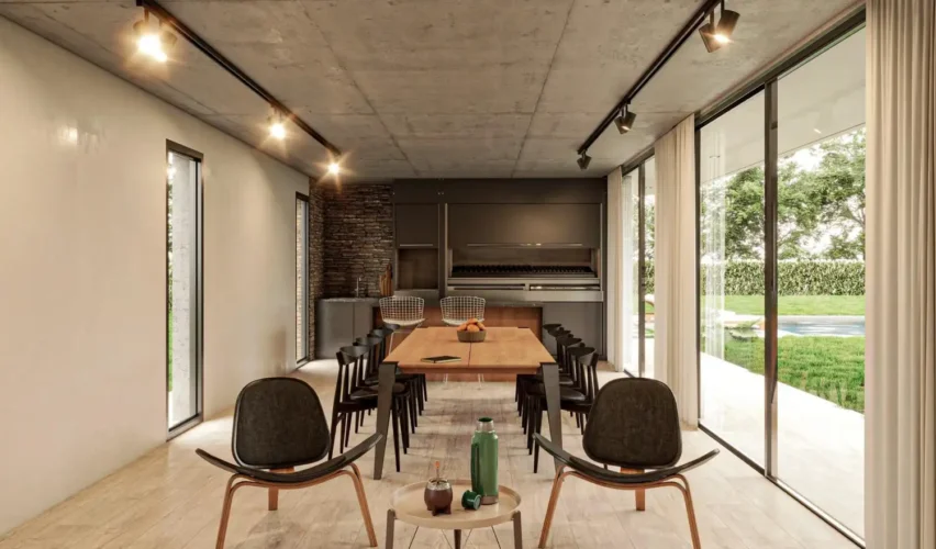 Ambiente externo moderno com mesa de jantar e poltronas, iluminação em trilho eletrificado preto no teto e refletor direcionável em fachada com grandes portas de vidro e jardim ao fundo.