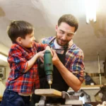 Pai e filho na oficina fazendo um trabalho de marcenaria, usando uma furadeira e peças de madeira; ideias de presentes para o dia dos pais