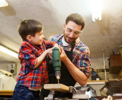 Pai e filho na oficina fazendo um trabalho de marcenaria, usando uma furadeira e peças de madeira; ideias de presentes para o dia dos pais