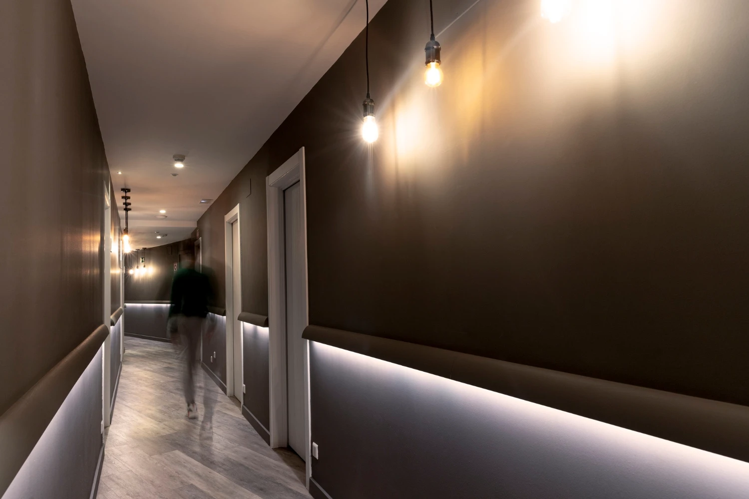 Corredor interno moderno com iluminação pendente e luzes acesas, sugerindo automação por sensor de presença para lampada para acionar a iluminação conforme a movimentação.