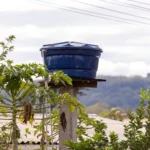 tanque fortlev instalado em área rural, com reservatório azul sobre base de concreto, cercado por plantas e vista para montanhas ao fundo