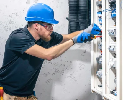 padrao trifasico: Técnico eletricista com capacete e luvas realizando manutenção elétrica em um painel de distribuição, com componentes internos e cabos visíveis ao lado de um gabinete industrial
